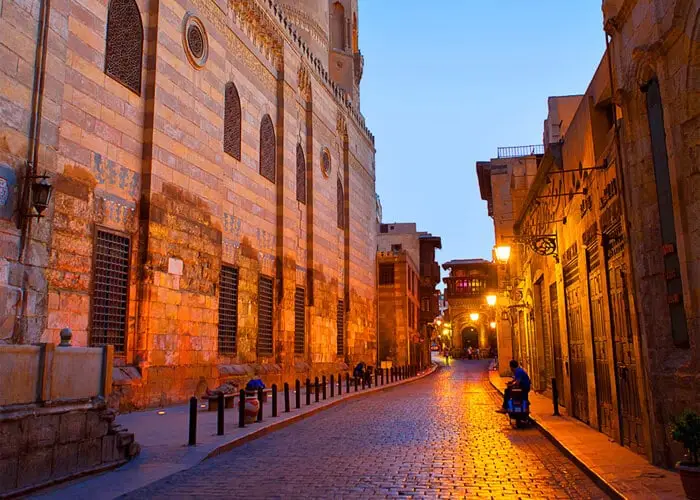 The architectural splendor of Al-Muizz Street in Islamic Cairo, showcasing a dense row of Mamluk and Fatimid minarets and stone-carved mosque facades under a clear sky.